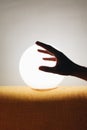 Vertical closeup shot of a hand silhouette in front of a moon-shaped lamp on a yellow tablecloth