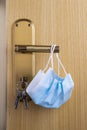 Vertical closeup shot of a medical face mask handing from a door handle with keys in the keyhole Royalty Free Stock Photo