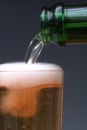 Vertical closeup shot of the pouring of the beer in the glass from the bottle with a dark background Royalty Free Stock Photo