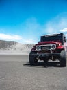 Vertical closeup shot of a red Jeep land cruiser on a sandy surface under the sunlight