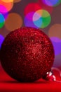 Vertical closeup shot of a red sparkly Christmas tree ball against the colorful bokeh lights Royalty Free Stock Photo