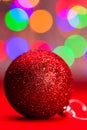 Vertical closeup shot of a red sparkly Christmas tree ball against the colorful bokeh lights Royalty Free Stock Photo