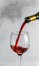 Vertical closeup shot of red wine being poured into a wine glass with grey background Royalty Free Stock Photo