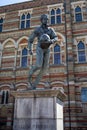 Vertical closeup shot of the sculpture of William Webb Ellis in front of a building on a sunny day