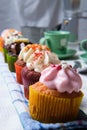 Vertical closeup shot of small cupcakes with colorful creams in a row on a kitchen towel Royalty Free Stock Photo