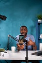 Vertical closeup of smartphone filming influencer sitting down at desk with laptop smiling