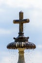 Vertical closeup of a stone cross on the top of a fountain against cloudy sunlit sky background