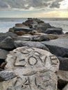 Vertical closeup of stone line carved the text "love", sea waves making foam, sunlit sky background