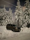 Vertical closeup of a SUV Jeep Commander on a snow-covered field, with pine trees in the background