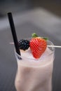 Vertical closeup of a transparent glass with fresh milk shake with strawberry and blackberry decorated with berries on a