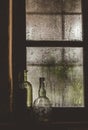 Vertical closeup of vintage glass bottles on a windowsill next to a steamy window in the dark Royalty Free Stock Photo