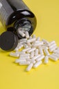 Vertical closeup of white pills spilled from a black tube on a yellow background Royalty Free Stock Photo