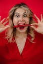 Vertical comical and funny expressive blonde woman holding red chili pepper in open mouth with bug eyes in red studio Royalty Free Stock Photo