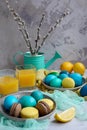 Vertical composition for Easter. Painted yellow, blue, green eggs on plates with macaroons and lemons on a light Royalty Free Stock Photo