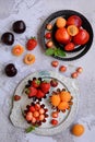 Vertical composition. Juicy ripe berries and fruits on metal plates on a gray textured background. View from above.