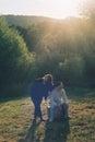 Vertical of a couple male sitting on a vintage TV and a female near sunlit landscape view background