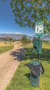 Vertical crop Pet Waste station with dog poop bags and garbage can beside a tree and pathway