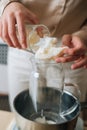 Vertical cropped shot of female artisan adding white dry soy wax in glass jar into pot of boiling water for creating