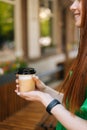 Vertical cropped shot of smiling redhead young woman holding cup with hot coffee sitting at table in outdoor cafe Royalty Free Stock Photo