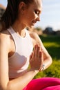 Vertical cropped shot of smiling young woman sitting on green grass with closed eyes in lotus position and holding hands Royalty Free Stock Photo