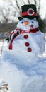 Vertical of a cute 6ft tall snowman with a black hat, carrot nose and a red scarf on a winter day