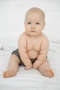Vertical cute infant naked baby in gray diaper, nappy sitting in light bedspread. Hygiene clothes, activity disposable