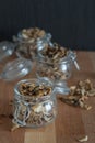 Vertical dark photo of sliced, chopped and dried various mushrooms in three preserving glass bowls standing on wooden seat or