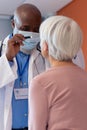 Vertical of diverse senior male doctor examining eye of female patient with penlight, copy space Royalty Free Stock Photo