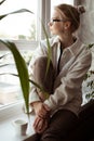 Vertical dreaming, tranquil, thoughtful blond woman in glasses and warm sweater sitting on windowsill with coffee mug Royalty Free Stock Photo
