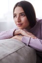 Dreamy young girl in sweater looking side, sitting on sofa Royalty Free Stock Photo