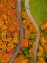VERTICAL: Drone shot of cars driving around vivid autumn colored countryside Royalty Free Stock Photo
