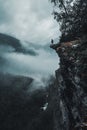 Vertical drone shot of a man on the edge of a rocky cliff facing the foggy forests