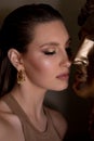 Vertical elegant fashionable brunette woman with close eyes, studio makeup near portrait sculpture Apollo. Spa skin care