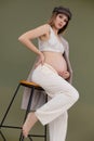 Vertical fashionable pretty pregnant barefoot woman cap, lace clothes, sitting bar stool. Touching abdomen, childbirth Royalty Free Stock Photo