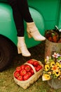 Vertical of a female in beige boots sitting on a green truck, near a basket of bell peppers
