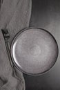 Vertical flat lay of an empty gray plate with black cutlery and linen fabric on dark background. Royalty Free Stock Photo