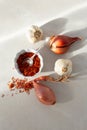 Cooking ingredients including garlic, dry shallots and safflower in small white dish on pale background