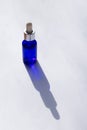 Vertical format photo of sunlit blue bottle with facial serum on white background with long shadows. Spa
