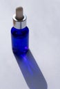 Vertical format photo of sunlit blue bottle with pipette full of facial skin care serum on white background with long shadows