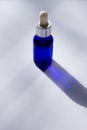 Vertical format photo of sunlit blue bottle with skin care serum on white background with long shadows. Spa treatment