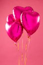 Vertical of four shiny pink heart shaped balloons floating on white background with copy space