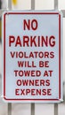 Vertical frame Close up of No Parking sign on awhite metal gate with building in the background