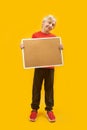 Vertical frame full-length portrait of blond boy with cortical board in his hands, yellow background. Place to advertise. Copy Royalty Free Stock Photo