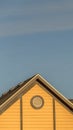 Vertical frame House exterior with roof shingles and round gable window against blue sky Royalty Free Stock Photo