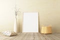 Vertical frame mockup standing on wooden floor in living room interior with dried plant, woven basket and pillow on concrete wall