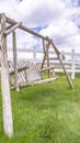 Vertical frame Old wooden garden swing on lush green grasses inside white picket fence Royalty Free Stock Photo