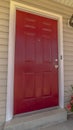Vertical frame Shiny red wooden front door of a home with wicker chairs on the sunlit porch Royalty Free Stock Photo