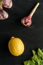 Vertical frame of two onions of garlic and lemon on a black background with fresh herbs. Royalty Free Stock Photo