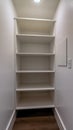 Vertical frame Walk in closet or pantry with empty wall shelves seen through open hinged door