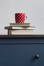 stack of closed books with tea cup on top on blue chest of drawers Royalty Free Stock Photo
